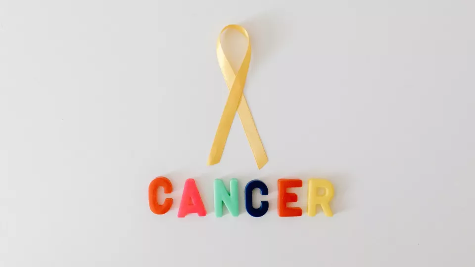 Foto på ett gult sidenband med färgglada plastbokstäver undertill som stavar ordet cancer