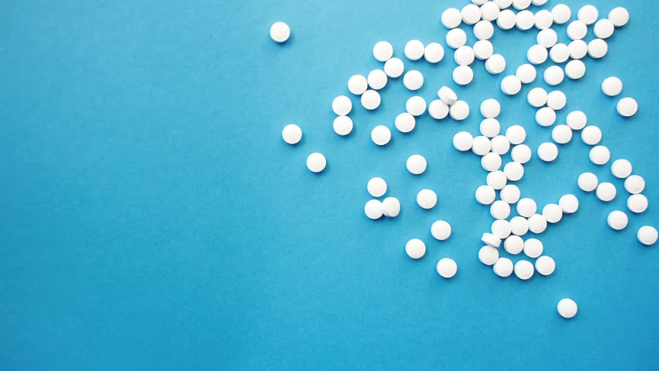 Foto på små vita runda tabletter mot en blå bakgrund.