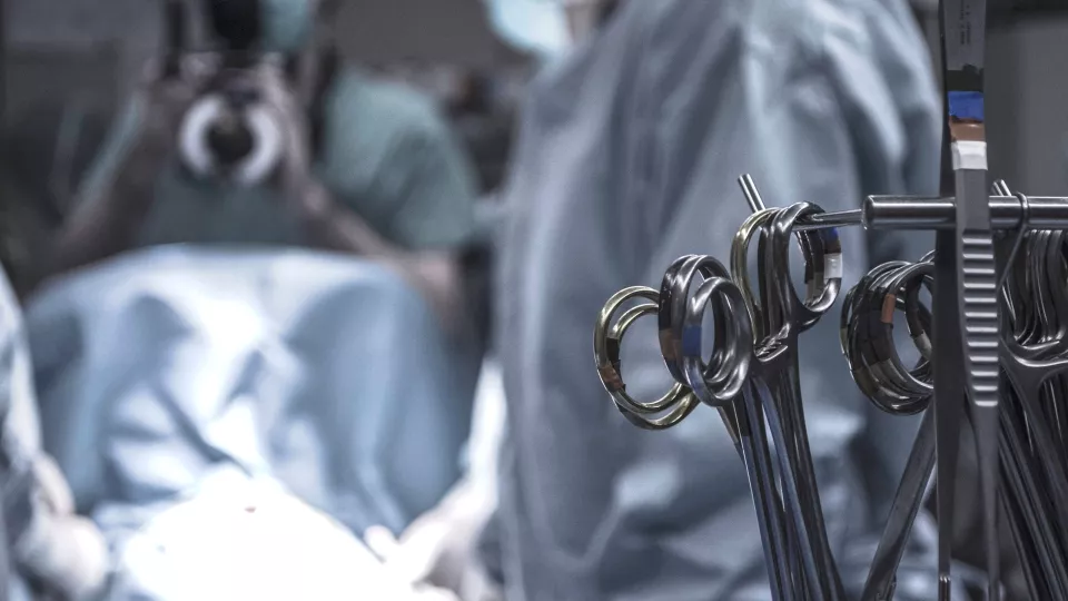 Ett operationsbord med en läkare i rock som opererar i bakgrunden. I förgrunden ses ett antal operationssaxar.