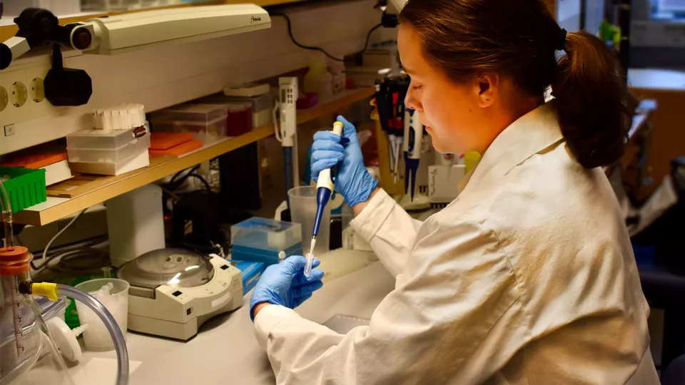 Amanda iklädd vit labbrock och blå handskar under tiden hon arbetar i labbet. 