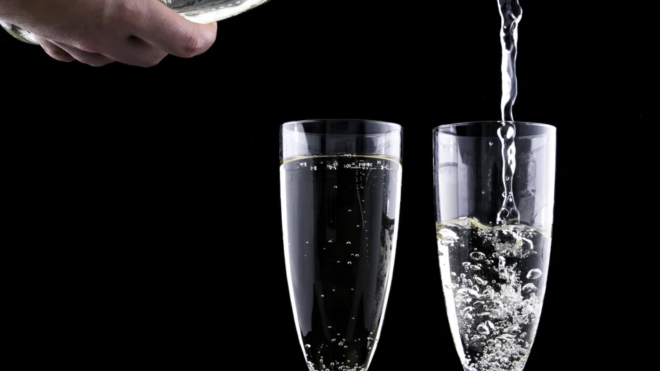 Närbild på två champagneglas och en flaska som häller upp dricka i ett av glasen.