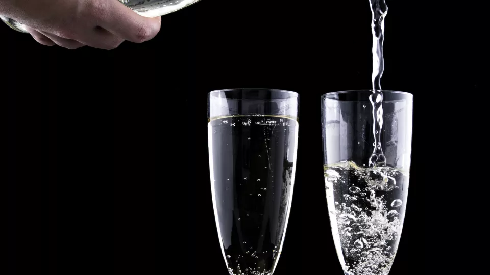 Närbild på två champagneglas och en flaska som häller upp dricka i ett av glasen.