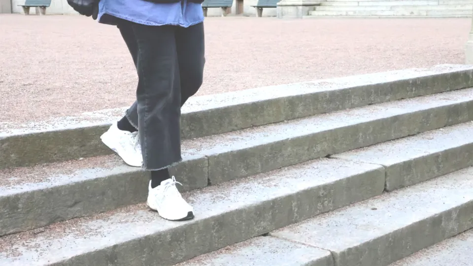 Halvkroppsbild, person i svarta byxor och vita skor som går nedför en trappa