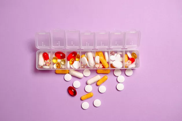 Foto på doseringsask med olika sorters tabletter i. Asken ligger mot en rosa bakgrund.