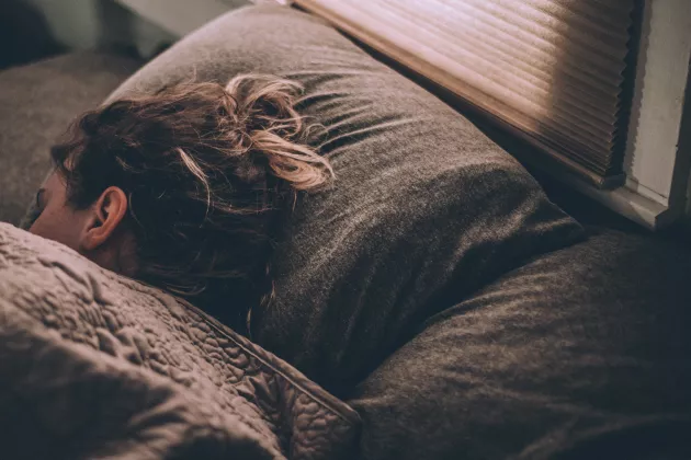 Foto på en kvinna med brunt hår som sover i en säng på en brun kudde med ett brunt täcke över sig.