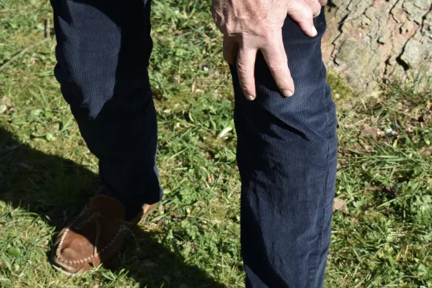 Person klädd i jeans som håller två händer på ett knä.