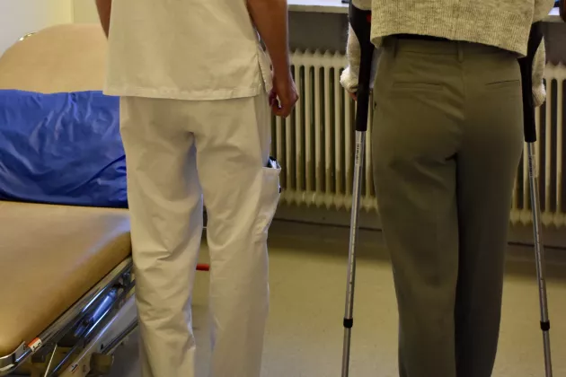 Bild bakifrån på en person med kryckor bredvid en vårdpersonal i vita kläder 