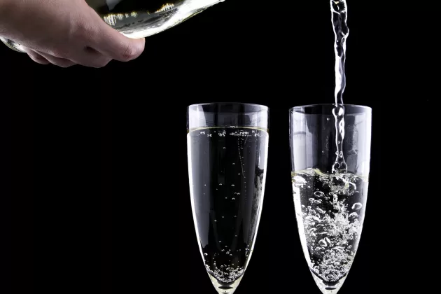 Närbild på två champagneglas och en flaska som häller upp dricka i ett av glasen.
