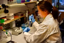 Amanda iklädd vit labbrock och blå handskar under tiden hon arbetar i labbet. 