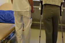 Bild bakifrån på en person med kryckor bredvid en vårdpersonal i vita kläder 