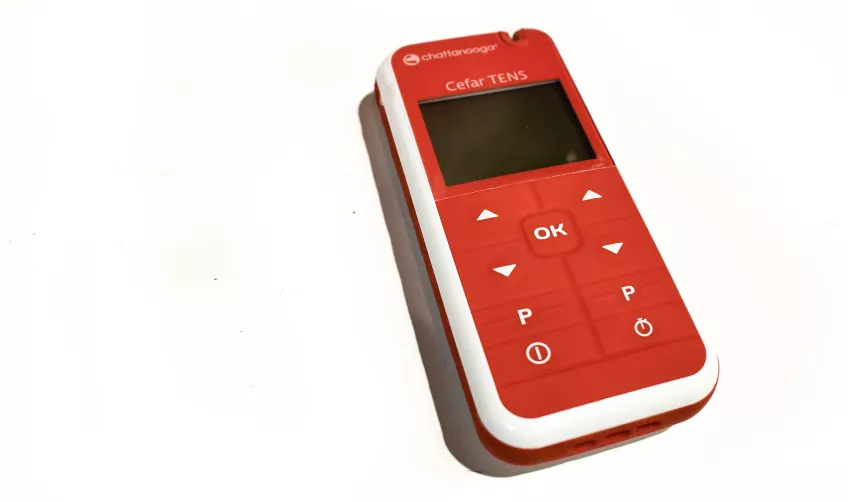 En röd TENS apparat som ligger mot en vit bakgrund.