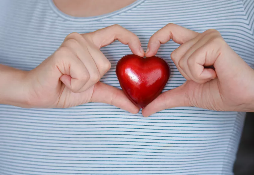 En person i en vit och blå randig t-shirt håller upp ett rött hjärta mot sitt bröst samtidigt som att pekfingrarna formats till ett hjärta.
