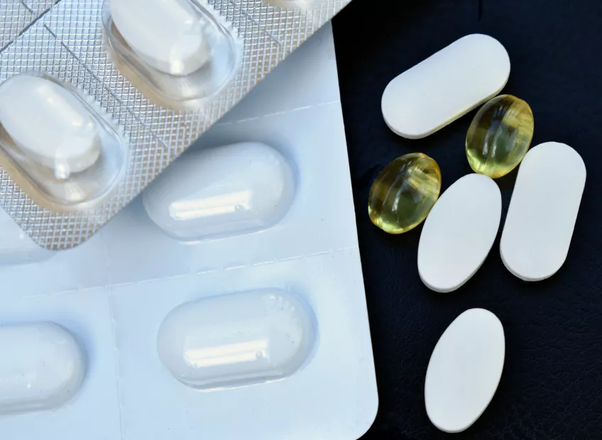 Fyra vita och två gula smärtstillande tabletter ligger bredvid en vit karta med tabletter på en svart bakgrund.