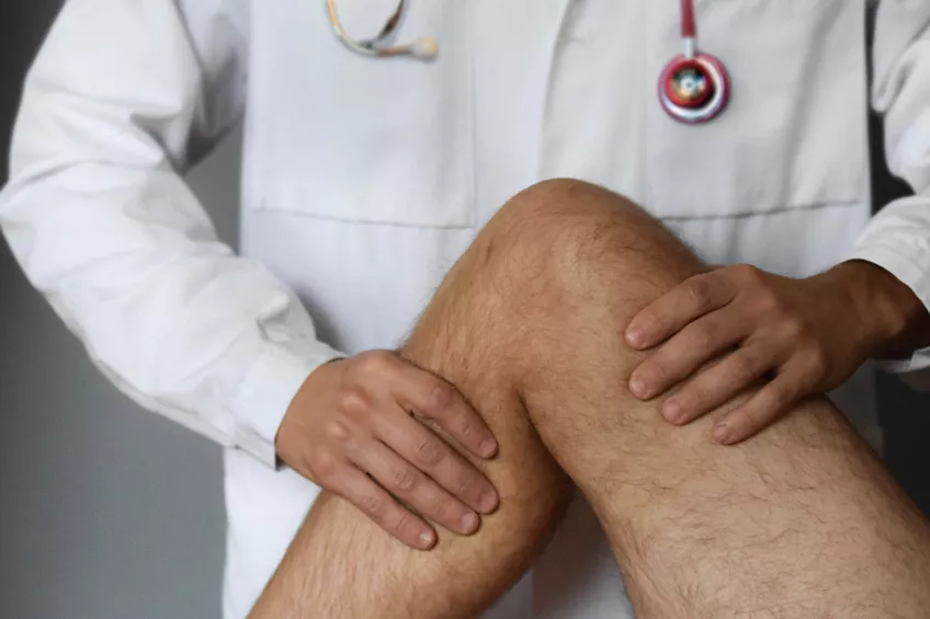 En läkare i vit rock med ett stetoskop runt nacken undersöker ett knä