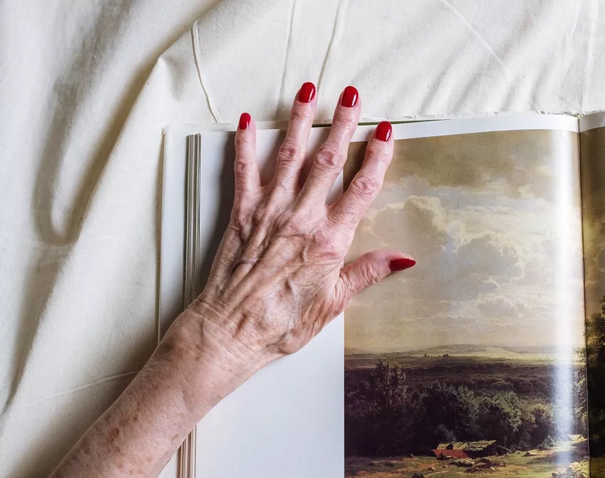 En reumatisk hand med rött nagellack vilar på en bok