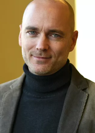 Porträttbild på Martin Englund. Martin är en vit man och har på sig en grå polotröja och en grön kavaj.